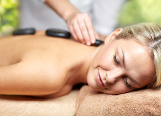 beauty, wellness and relaxation concept - close up of beautiful young woman having hot stone massage in spa over green natural background