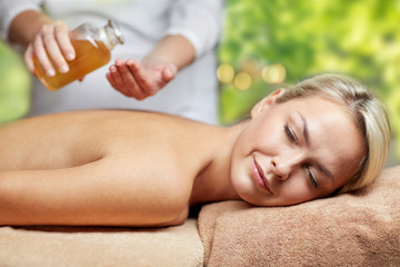 Obraz na płótnie Canvas beauty, wellness and relaxation concept - close up of beautiful young woman lying with closed eyes on massage table and therapist holding oil bottle in spa over green natural background