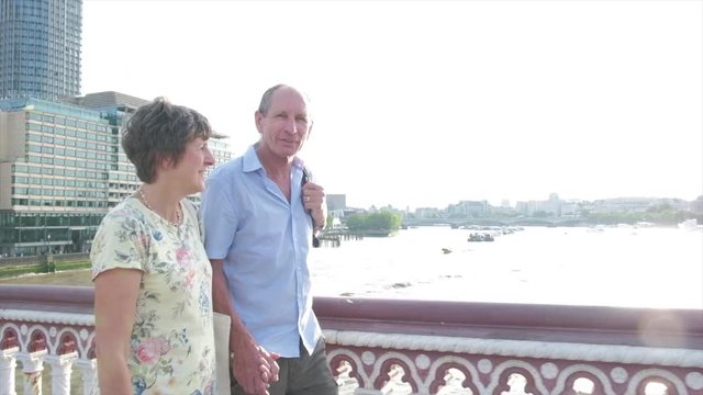 Slow motion steady cam view of active senior caucasian tourist couple walking in on blackfriars bridge london with the river thames behind themes of sightseeing active seniors direction on the move