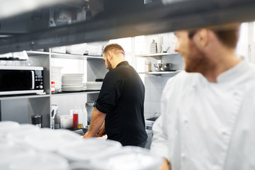 cooking food, profession and people concept - happy male chef and cook at restaurant kitchen