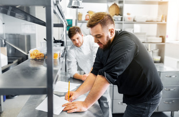 cooking food, profession and people concept - happy male chef and cook with grocery lists or bills...