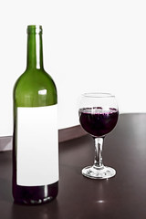 Open bottle and one glass of red wine on brown wodden table and white blurred wall background. Alcohol drink on desk in room. Mockup for wine label
