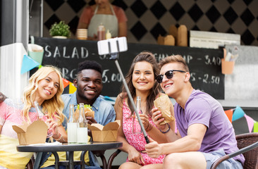 leisure, technology and people concept - happy young friends with food and non alcoholic drinks and taking selfie at food truck