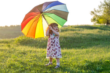 Beautiful girl plays on nature with a colorful umbrella. Rainbow umbrella in the hands of the child