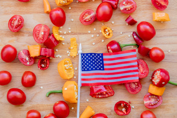 Naklejka na ściany i meble cut tomatoes with yellow and red peppers with US flag on wooden table. Above view