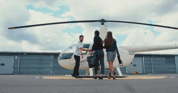 Commercial pilot in uniform greeting clients near small private helicopter on a landing point. 4K UHD