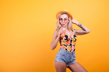 Attractive young woman drinking orange juice with sunglasses in studio