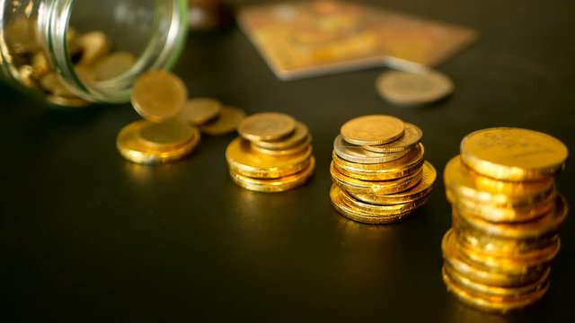 Saving money coin from jar. Symbol of investing, keeping money concept. Collecting cash conis in glass tin as moneybox. Close-up still life with increasing columns of gold coins on black table