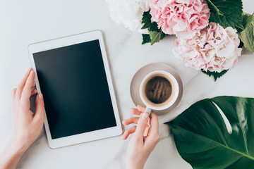 cropped view of woman hand with coffee cup and digital tablet with blank screen on tabletop with hortensia flowers