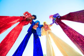 Young people on stilts posing against the blue sky.