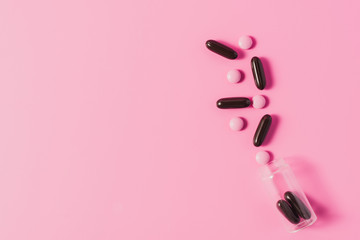 top view of bottle with spilled pink and black pills on pink