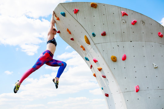 Photo of sportswoman in leggings hanging on wall for rock climbing against blue sky