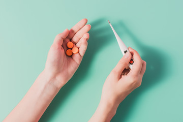 cropped shot of woman holding heap of pills and thermometer on blue