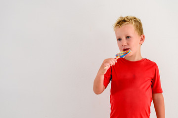 Boy with red shirt on white background eating a lollipop colorful fun and laughing.