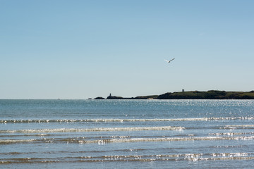 Harsh sunlight reflection on sea waves and Llanddwyn Island in the background on middy in hot summer