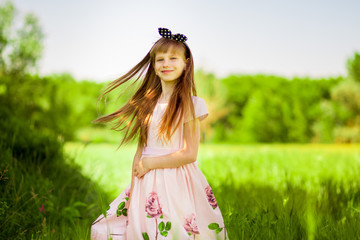 Portrait of beautiful little girl in elegant dress in middle of green summer field