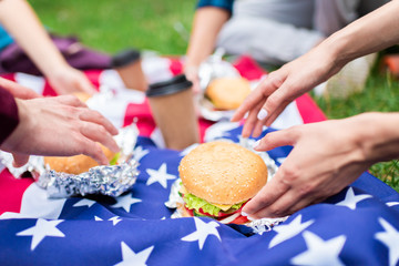 Obraz na płótnie Canvas partial view of friends with burgers and american flag on green grass in park