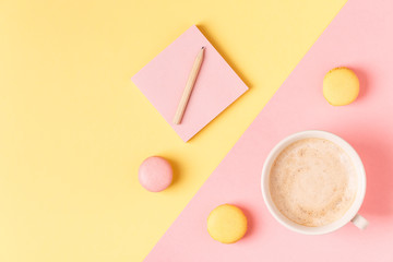 Cup of coffee with macaroons on pastel background.