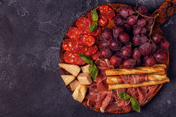Prosciutto, sausage, wine, grape, parmesan on dark table.