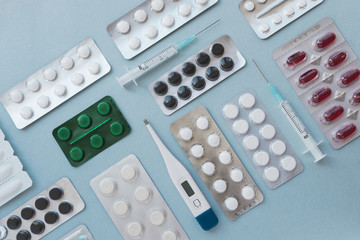 A lot of colorful medicine pills and blisters pack. Pharmaceuticals capsule pills medicine, antibiotics. Medical syringes, thermometer. Flat lay on blue background. 
