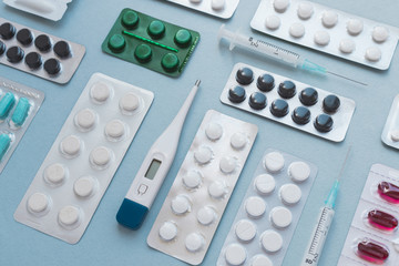 A lot of colorful medicine pills and blisters pack. Pharmaceuticals capsule pills medicine, antibiotics. Medical syringes, thermometer. Flat lay on blue background. 