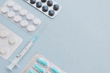 Different medicine drugs, pills, tablets in blister packages and medical syringe on blue background. With empty text space. Flat lay on blue background. 