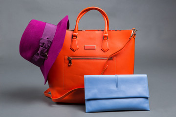 orange ladies bag, blue clutch and lilac felt hat on a gray background, concept of fashion accessories, purchases
