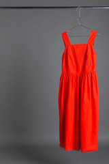 red summer dress hanging on a hanger on a gray background, concept of fashionable clothes and shopping