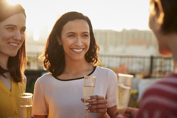 Female Friends With Drinks Gathered On Rooftop Terrace For Party With City Skyline In Background