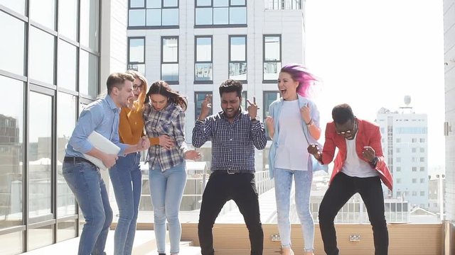 Group of multi ethnic young friends dressed in casual cloth having fun on lounge outdoor area on the roof of office glass building