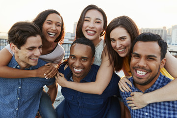 Portrait Of Men Giving Women Piggybacks On Roof Terrace With City Skyline In Background