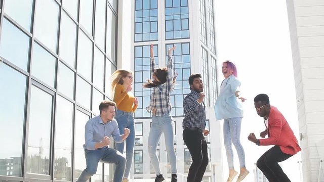 Group of multi ethnic young friends dressed in casual cloth having fun on lounge outdoor area on the roof of office glass building