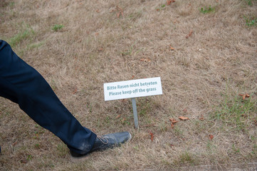 vertrockneter Rasen mit schild Rasen betreten verboten und Schuh Fuß