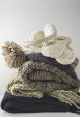 Fototapeta na wymiar Warm woolen knitted winter and autumn clothes, folded in a pile on a white table. Sweaters, scarves, gloves, hat, headphones. Place for text. Copyspace.