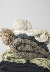 Fototapeta na wymiar Warm woolen knitted winter and autumn clothes, folded in a pile on a white table. Sweaters, scarves, gloves, hat, headphones. Place for text. Copyspace.