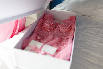 A young girl in a pink robe opens a white box with a bow with a new pink dress inside, unleashes a bow on the gift box. Surprise or gift on the bed in the bedroom.