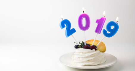 Pavlova cake with blueberries, raspberries and peaches and burning candles 2019 on bright white background in plate.