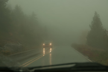 View from the windshield of the car on the road in a strong mist and the headlights of an oncoming...