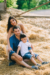 Fototapeta premium cheerful parents and son sitting on hay at village