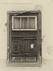 a sepia image of an old spanish shuttered window in a traditional house with faded plaster walls in strong sunlight