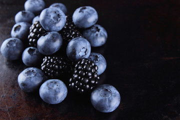 Blueberries and blackberries on dark background, fresh berries for vegan, fruits on rusty background, assorted berry breakfast