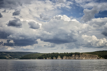Bright beautiful clouds. The bank of the river, on the horizon of the mountain and forest. . The warm summer and the beauty of nature. Soon it will start to rain.