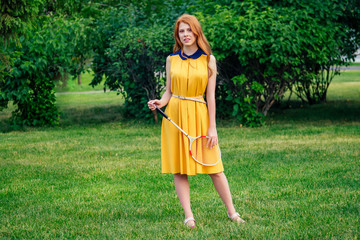 active cheerful beautiful young ginger redhead irish woman in a yellow dress and in a pink playing tennis badminton racket in the summer park