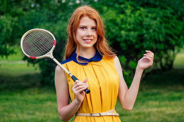 active cheerful beautiful young ginger redhead irish norwegian female person in a yellow dress and in a pink playing tennis badminton racket in the summer park