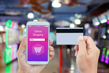 Hand holding smart phone with online shopping on screen and credit card over blurred in shopping mall background for mobile banking payment online concept