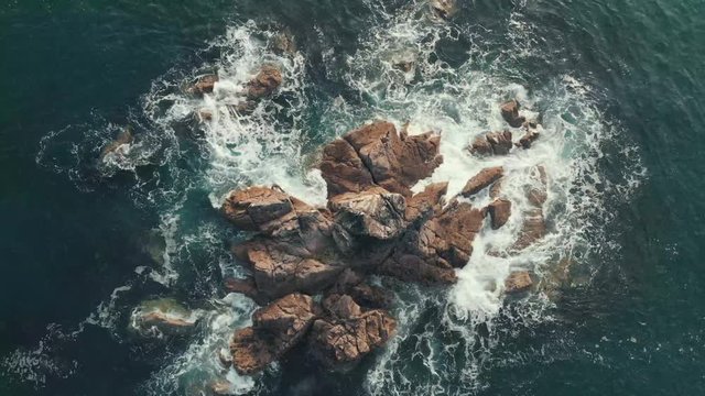 Aerial drone shot of waves crashing on cliffs & rocks