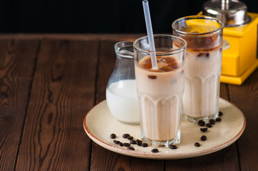 Iced coffee in a tall glass served on a plate on a wooden background.