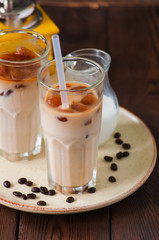 Iced coffee in a tall glass served on a plate on a wooden background.