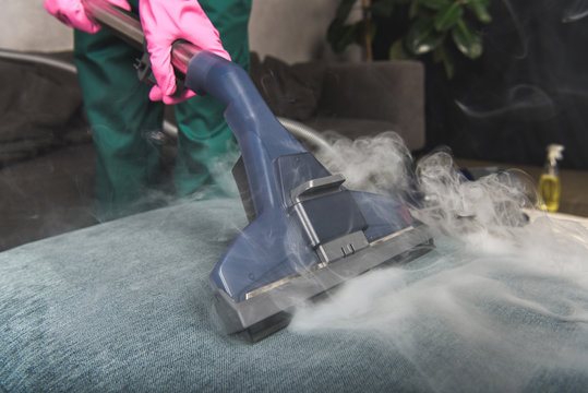 Cropped shot of person cleaning sofa with vacuum cleaner, hot steam cleaning concept