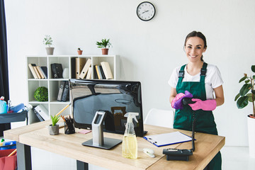 Beautiful young professional cleaner smiling at camera while cleaning modern office